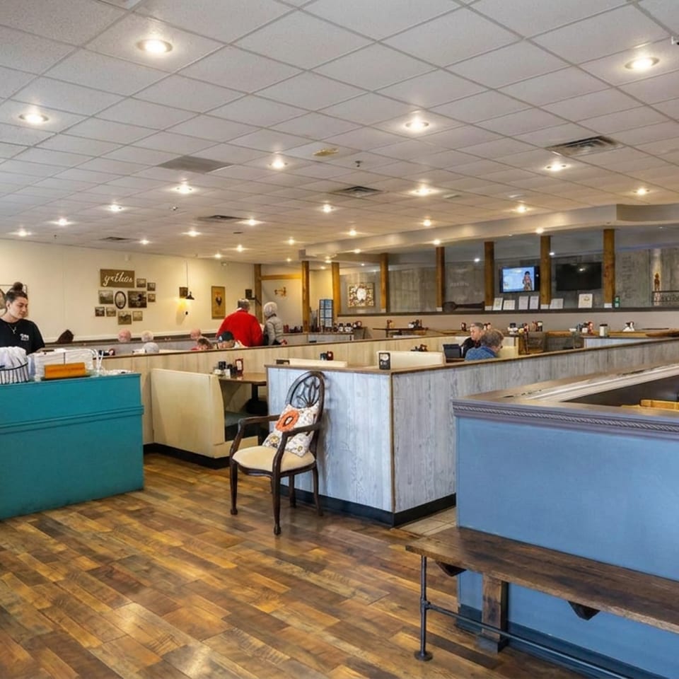 Spacious restaurant dining room with blue booths, wooden floors, pendant lights, artwork, and several seated diners.