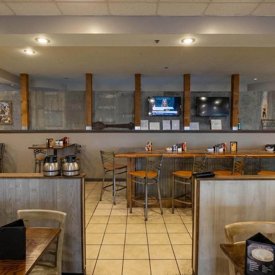 Warmly lit restaurant dining room with wooden tables, booths, bar seating, televisions, and rustic wood-paneled decor.