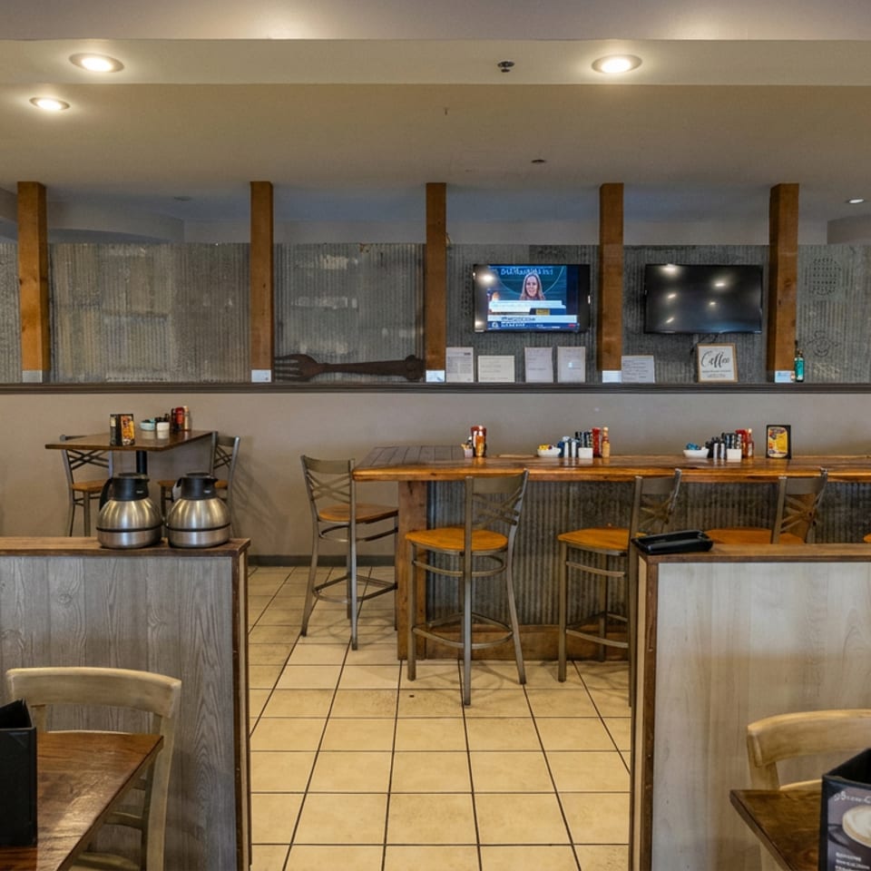 Warmly lit restaurant dining room with wooden tables, counter seating, coffee urns, televisions, and rustic decor.