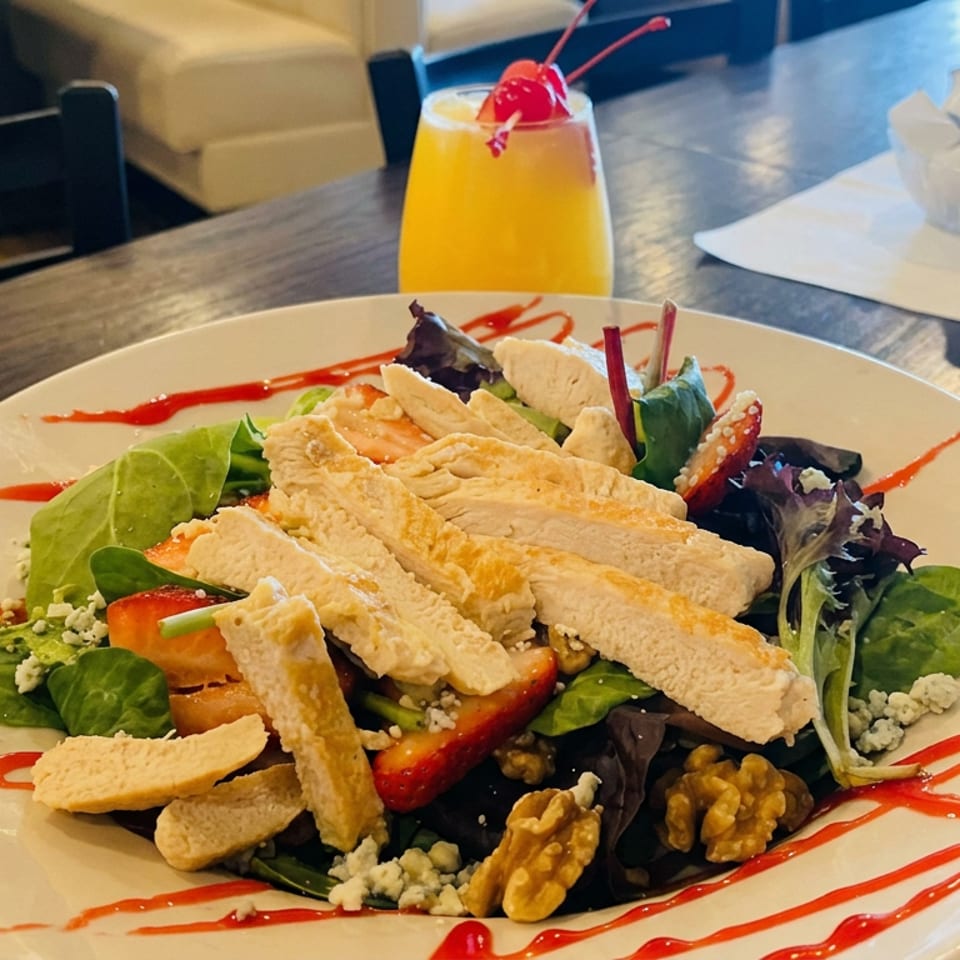 Mixed green salad topped with breaded chicken strips, strawberries, walnuts, blue cheese, and red sauce drizzle, served with an orange drink.